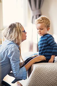 A young mother talking to her son inside in a bedroom.