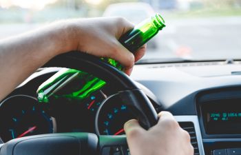 Drunk man driving a car with a bottle of beer.