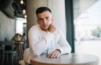 A worried young man sitting alone at an empty table in a cafe